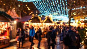 There are no shortage of Christmas markets in Sussex to enjoy this festive season. The image shows a blurred out Christmas market with fairy lights, stalls, and shoppers