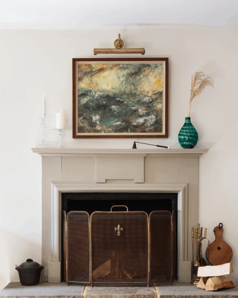 A beige stone, open log fireplace with a painting above the mantle piece.