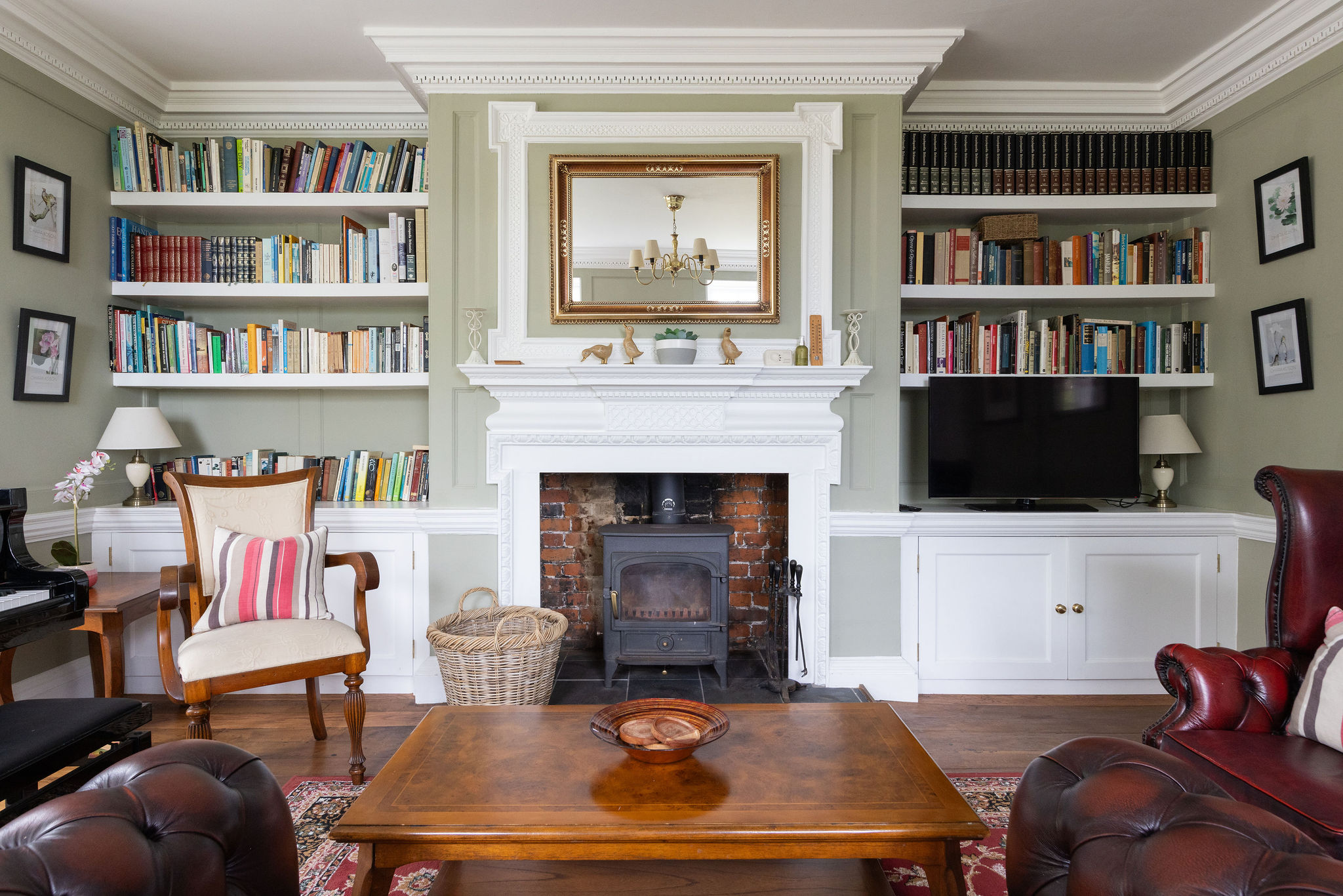 A cosy, elegant living room with built-in bookshelves, a central fireplace, leather armchairs, and a wooden coffee table.