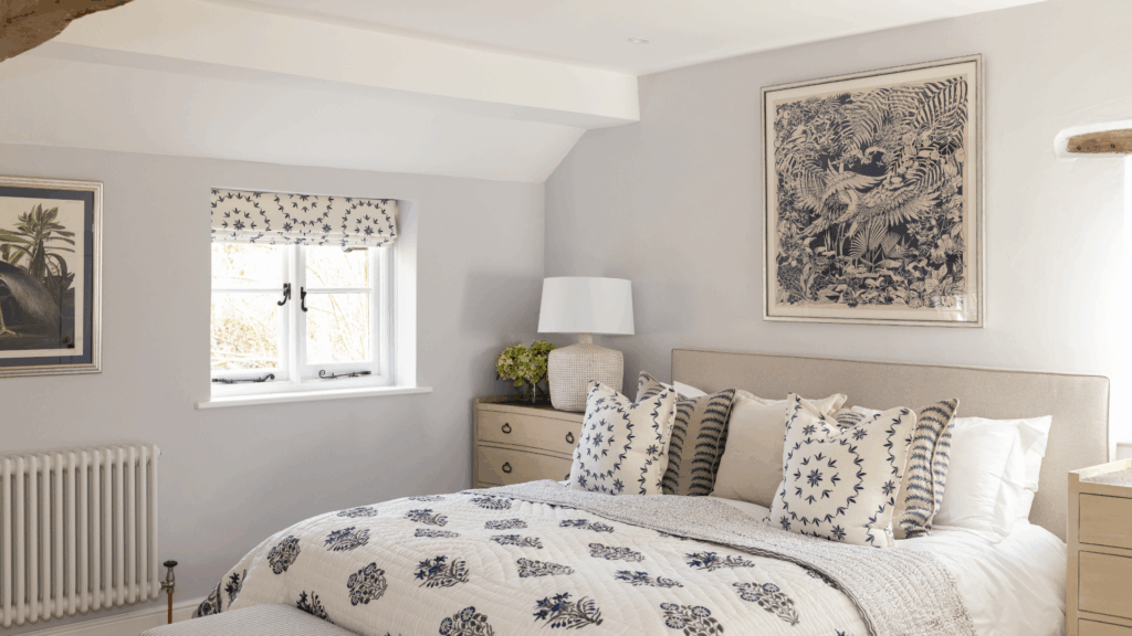 ht, neutral bedroom with a double bed dressed in blue and white patterned cushions and quilt, bedside lamp, and framed artwork on pale grey walls. Personalised Luxury Staycations.
