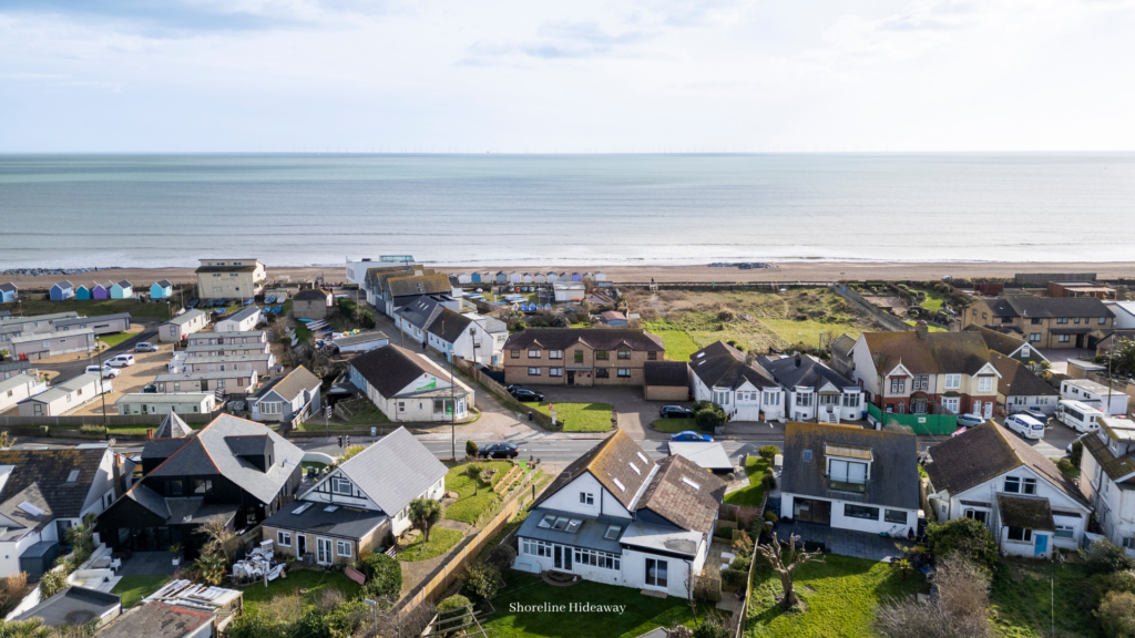 Aerial view of a coastal holiday home neighbourhood with beach huts, seaside homes, and the ocean stretching into the distance.