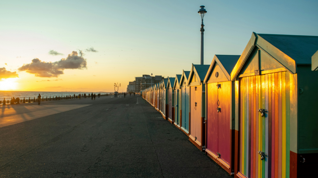 Colourful beach huts lining Brighton seafront at sunset with golden light reflecting across the promenade.