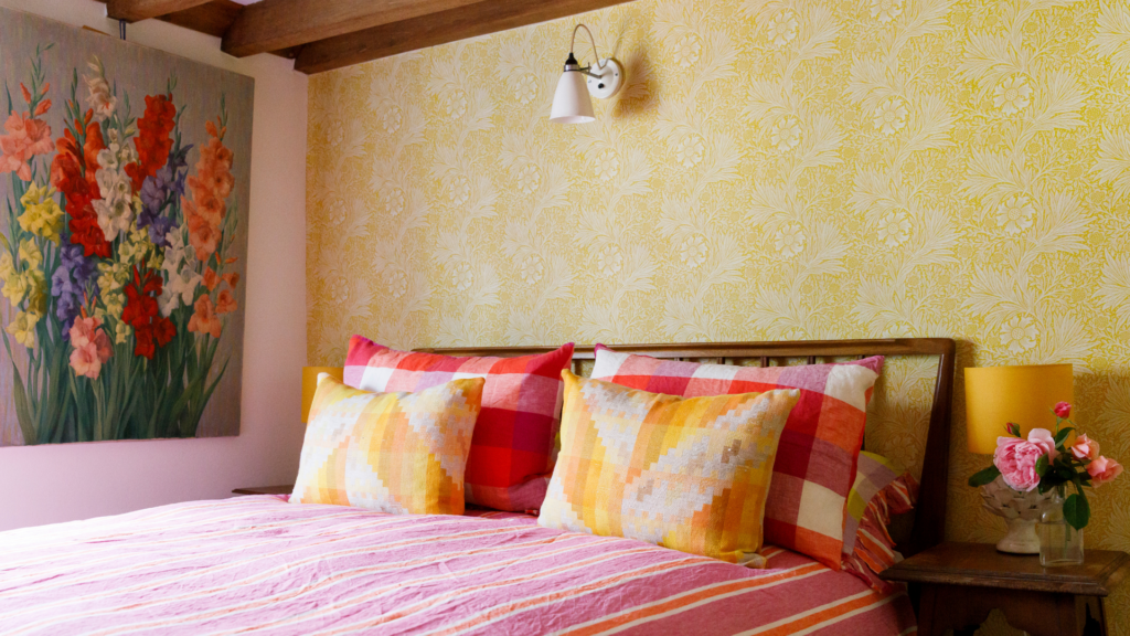 Bright, character-filled bedroom at 15 Bond Street featuring floral wallpaper, colourful cushions, wooden beams and thoughtful vintage styling.