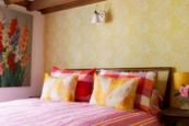 Bright, character-filled bedroom at 15 Bond Street featuring floral wallpaper, colourful cushions, wooden beams and thoughtful vintage styling.