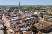 Aerial view of Chichester city centre, with Chichester Cathedral surrounded by historic rooftops, bustling streets and green countryside beyond.