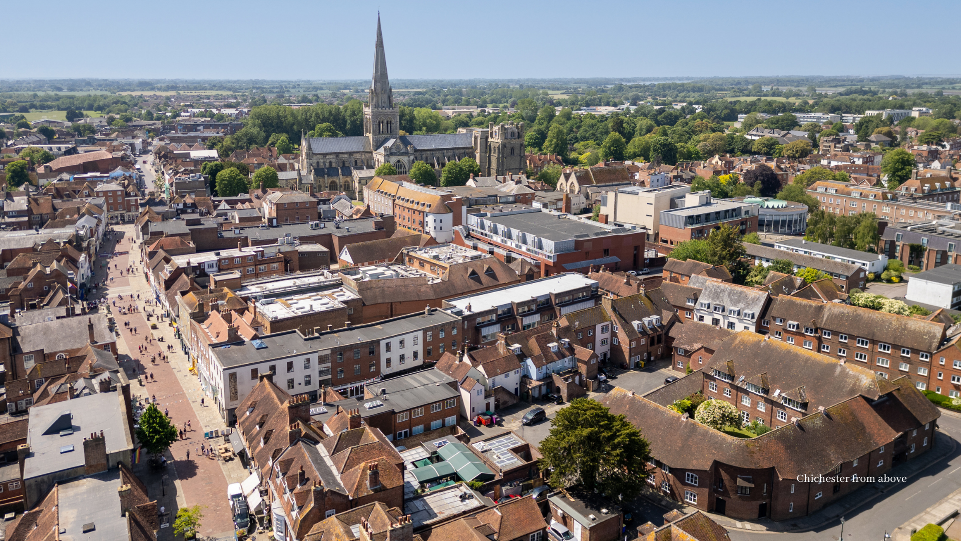Aerial view of Chichester city centre, with Chichester Cathedral surrounded by historic rooftops, bustling streets and green countryside beyond.