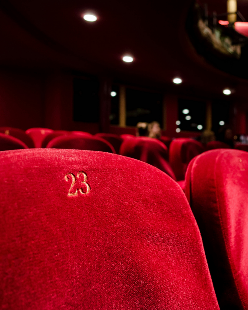 Close-up of plush red cinema seats inside an intimate theatre, with seat number 23 in focus and soft ambient lighting.