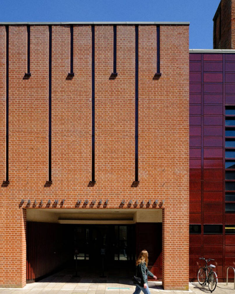 Exterior of Chichester Cinema, featuring its distinctive brick facade on a sunny day with a pedestrian walking past the entrance.