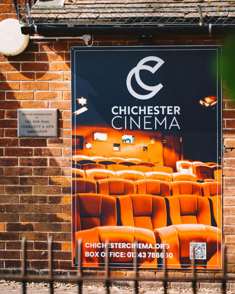 Chichester Cinema promotional sign mounted on a brick wall, featuring rows of plush cinema seats and venue branding.