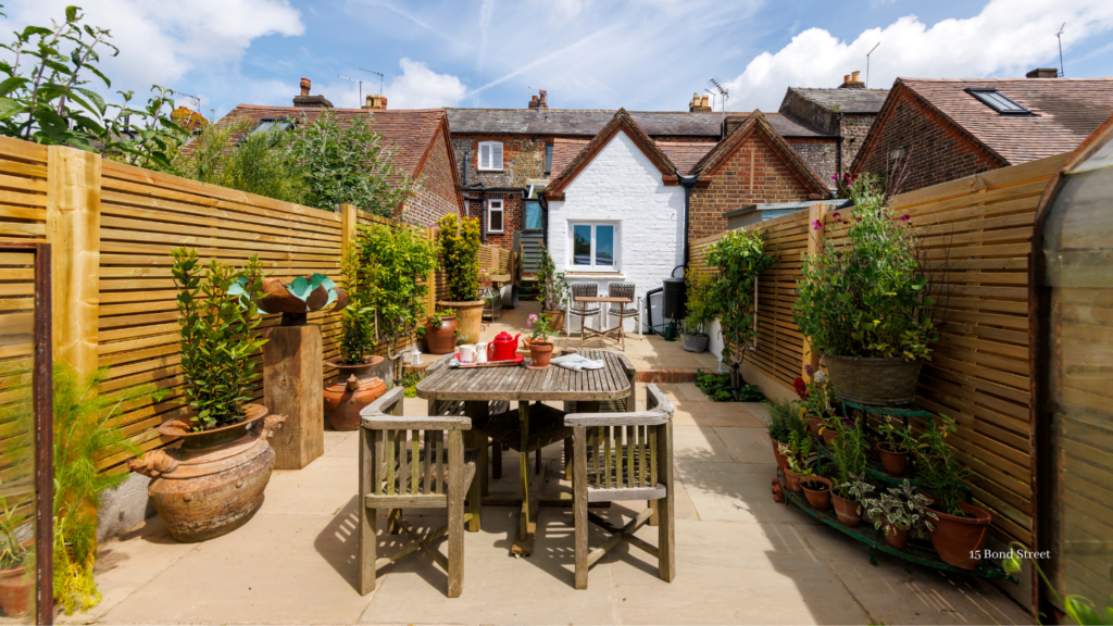 Private courtyard garden with outdoor dining table, potted plants and patio seating behind a charming brick holiday cottage on a sunny day.