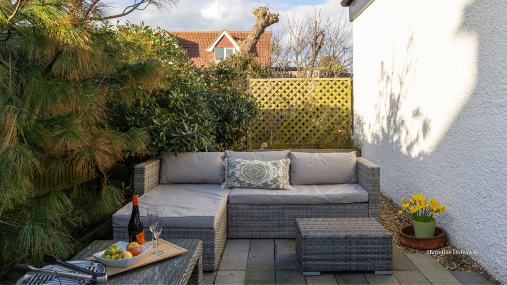 Cosy private patio with cushioned outdoor sofa, coffee table and garden seating, surrounded by lush greenery in the afternoon sun.